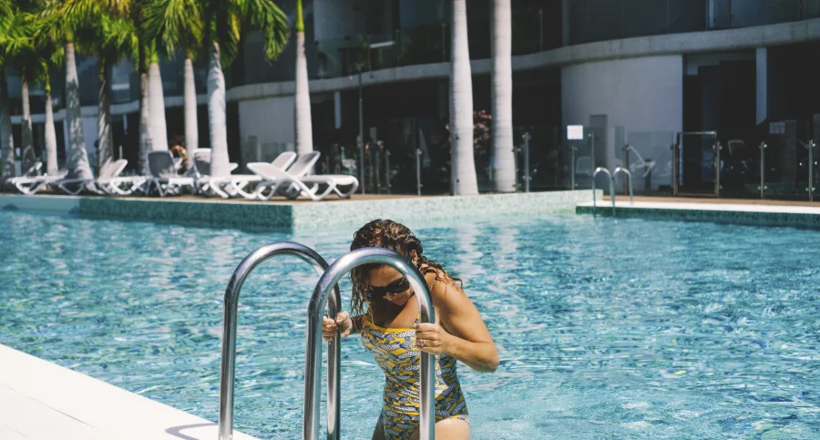 Envato - One rich lady going out from a big blue pool after swimming or relaxing in summer leisure activity. Resort hotel in background. Luxury lifestyle peopl